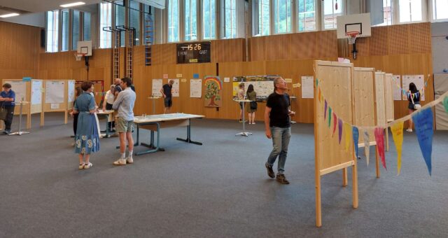 Mehrere Personen in einer Turnhalle mit Aufstellern zur nachhaltigen Entwicklung der Gemeinde Großarl.