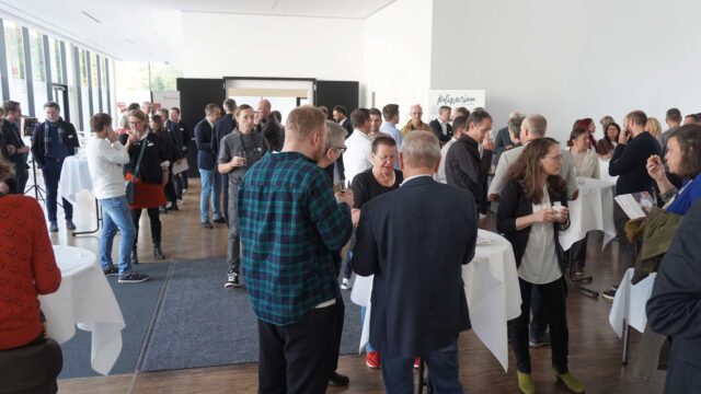 Viele Menschen stehen an Stehtischen und unterhalten sich