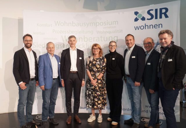 Acht Personen stehen vor einem Fotohintergrund mit SIR-Logo