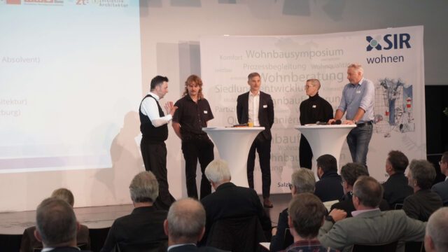 Vier Personen stehen auf einer Bühne an Stehtischen und unterhalten sich.