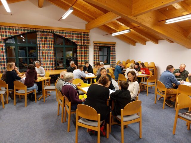 Rund zwanzig Personen sitzen in Kleingruppen an Tischen beieinander und sind im Gespräch