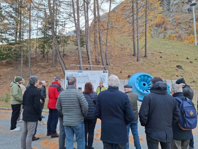 Eine Gruppe an Menschen steht vor dem Pumpspeicherkraftwerk und hört dem Vortragenden zu