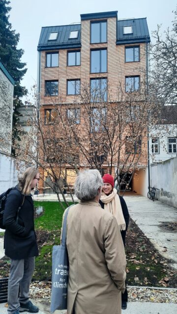 Personen stehen vor einem Gebäude mit Holzverkleidung