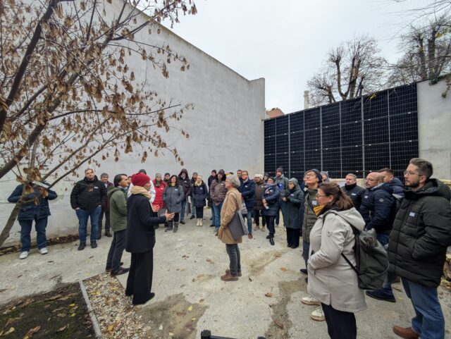Eine Gruppe von Menschen steht vor einem Gebäude und hört der vortragenden Person zu.