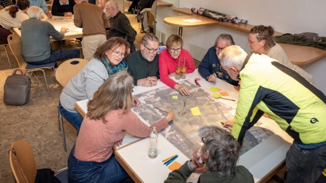 Personen sitzen um einen Raumplan herum