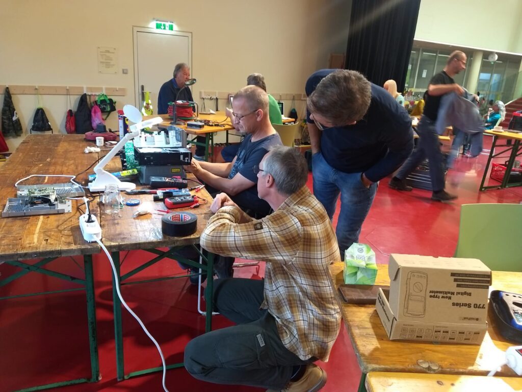 Menschen stehen an verschiedenen Repaircafé-Stationen
