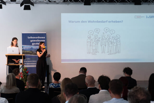 Sarah Untner hält ein Mikrofon in der Hand und spricht. Auf der Folie steht 