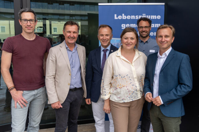 Sechs Personen stehen vor einem Rollup mit der Aufschrift 