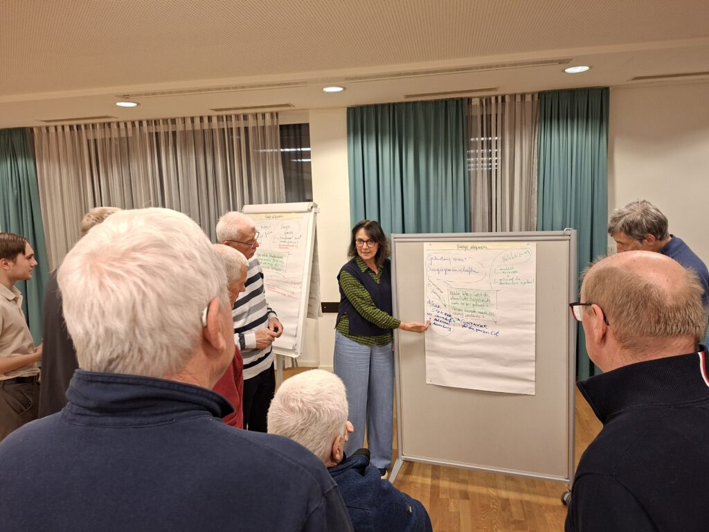 Eine Frau steht vor einer Pinnwand mit einem Plakat und zeigt auf das Plakat.