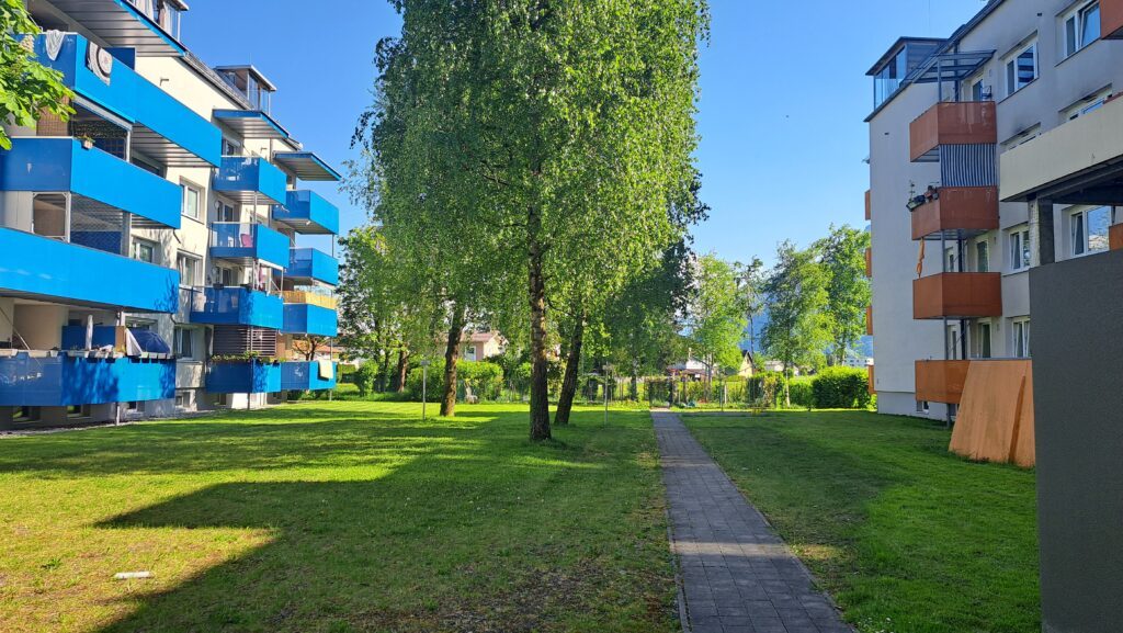 Links und rechts stehen zwei Wohngebäude, dazwischen ist eine Wiese