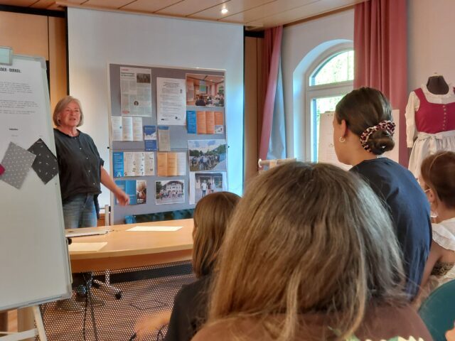 Eine Frau steht vor einer Pinnwand und spricht zum Publikum.