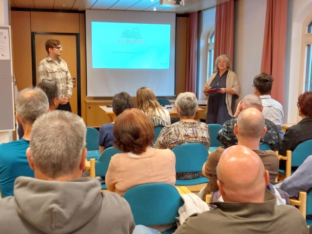 Ein Mann und eine Frau stehen vor eine Publikum und präsentieren.