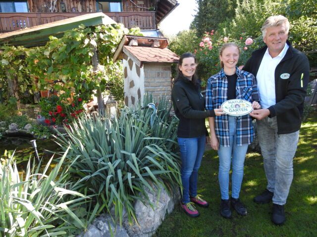 Zwei Frauen und ein Mann halten die Natur in der Gemeinde-Plakette in der Hand