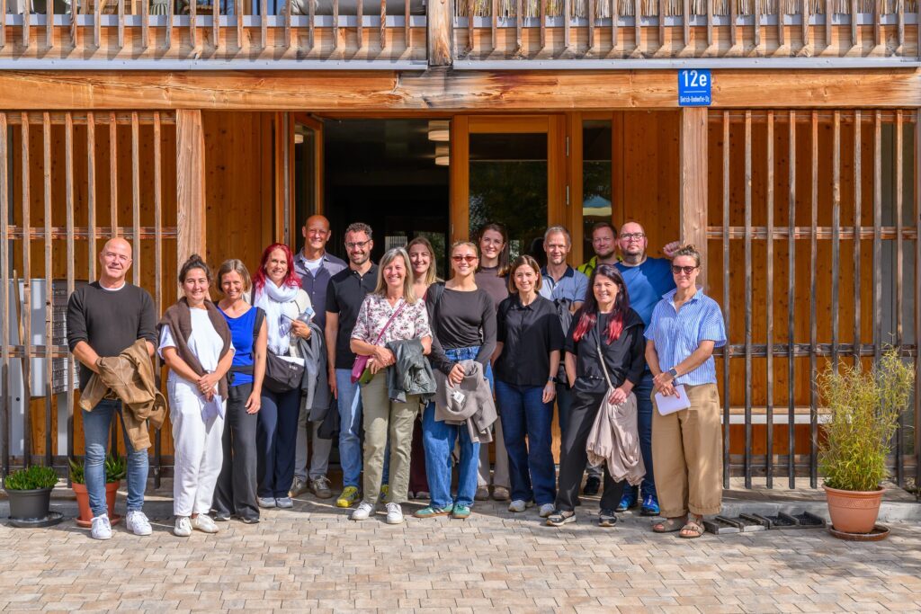 Gruppenfoto der Wohnbauexkursion mit vielen Menschen vor einem Haus mit Holzverkleidung.
