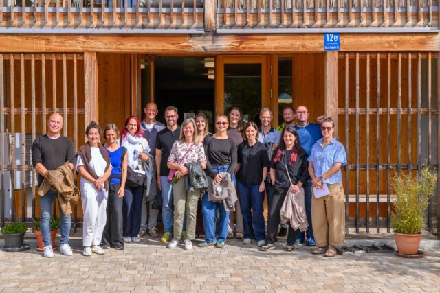 Gruppenfoto der Wohnbauexkursion mit vielen Menschen vor einem Haus mit Holzverkleidung.